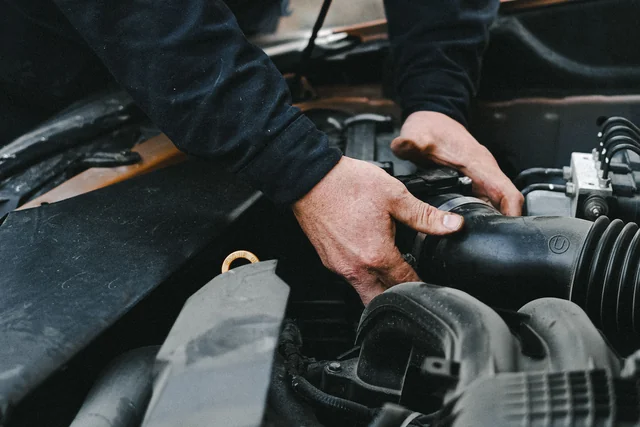 Hands adjusting an air intake hose in a car engine bay